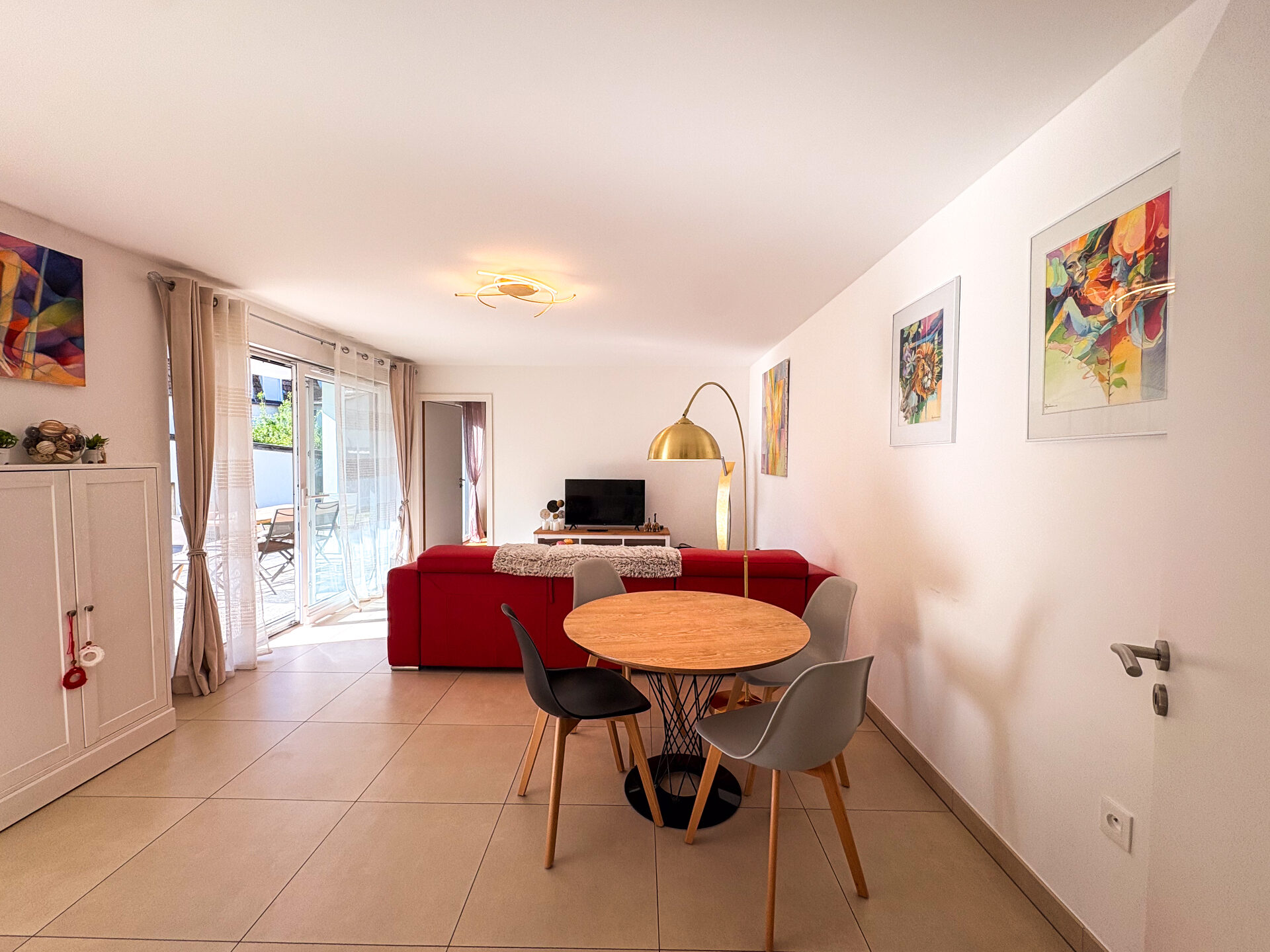 Séjour avec coin repas, canapé rouge et accès terrasse